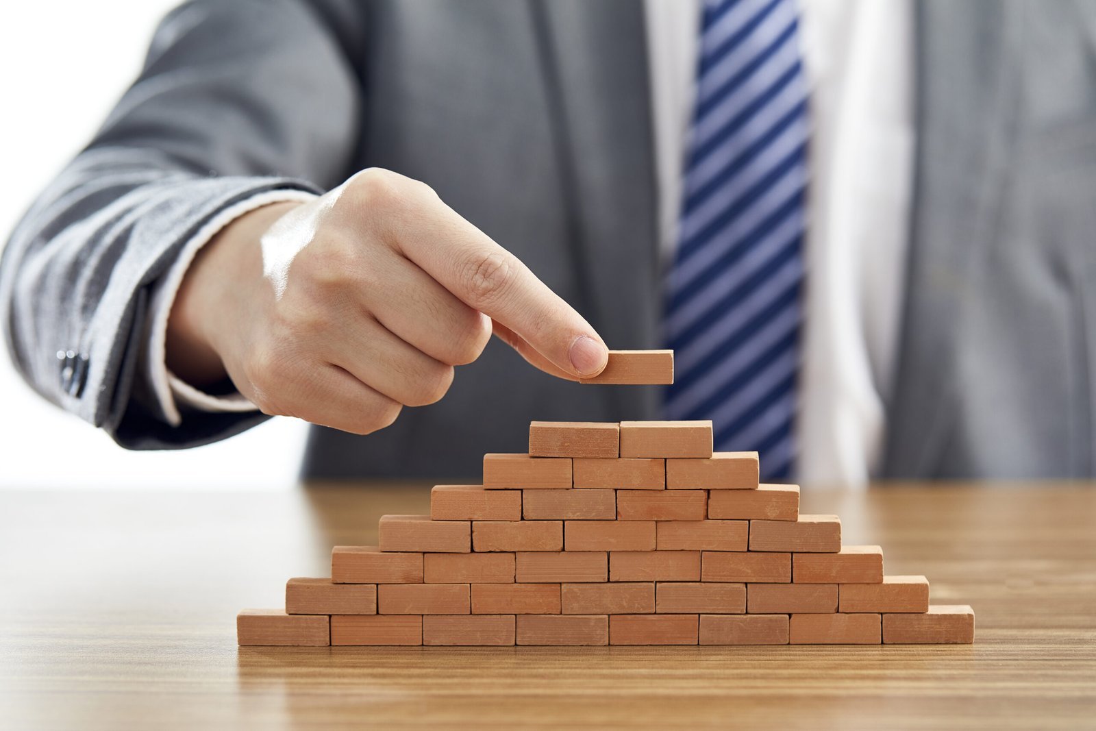 businessman-suit-putting-last-piece-pyramid-using-wooden-blocks-scaled.jpg